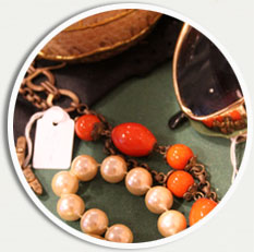Närbild på smycken. Ett pärlhalsband och ett halsband med pärlor som orange nypon syns.